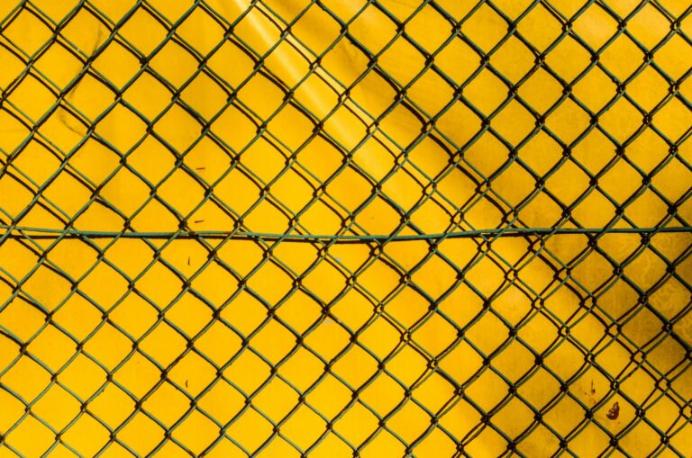 A close-up of a chain link fence against a bright yellow background, creating a stark contrast.