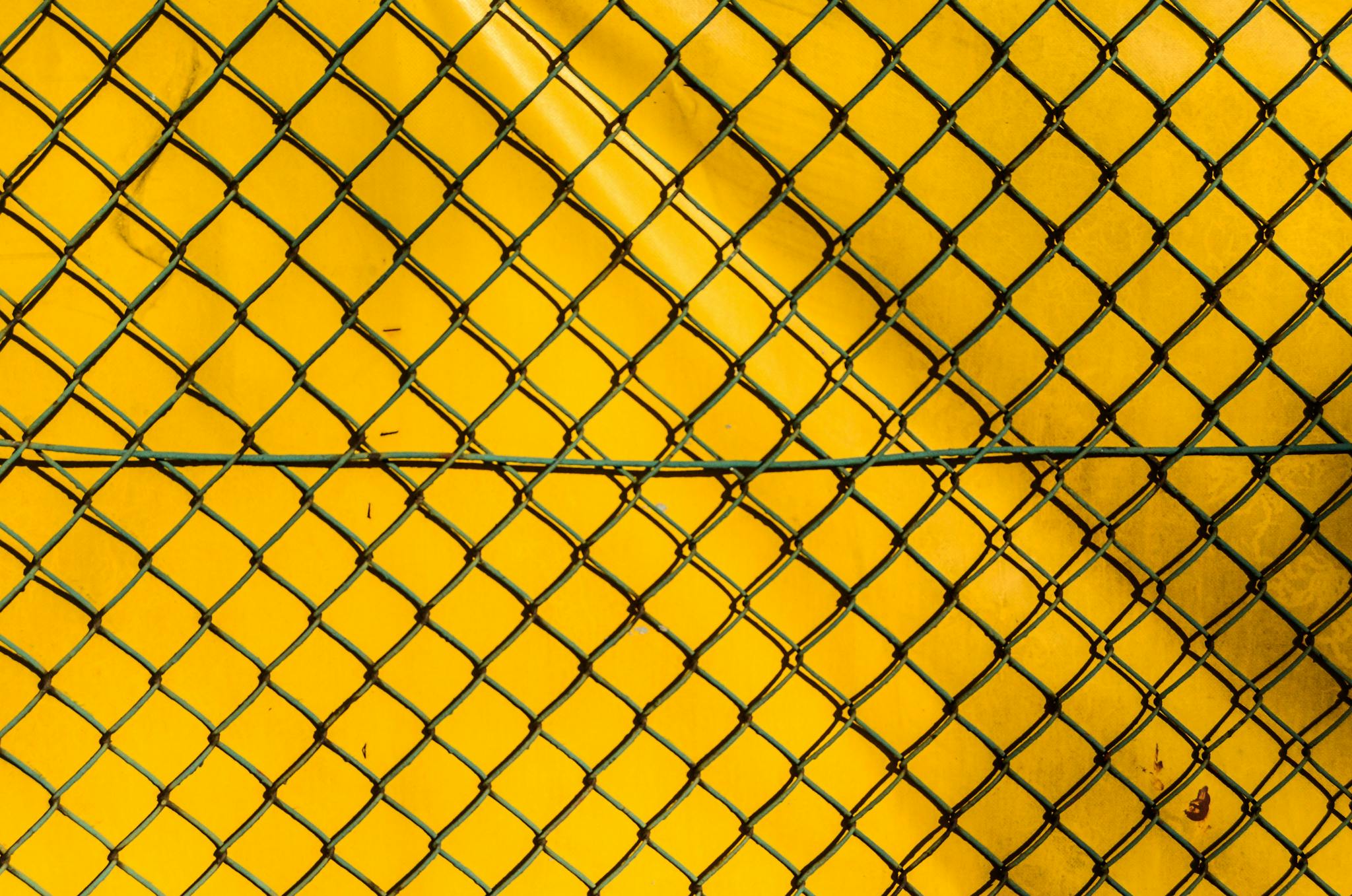 A close-up of a chain link fence against a bright yellow background, creating a stark contrast.