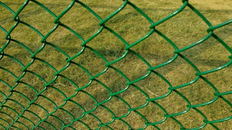 Close-up of a green wire fence with grassy background. Ideal for design and texture themes.